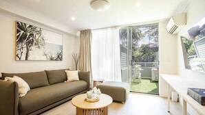 Uma sala de estar moderna com um sofá, uma mesa de centro e vista para um jardim através de uma porta de vidro deslizante.