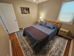 Un dormitorio con cama, mesita de noche, lámpara, ventana con persianas y puerta.