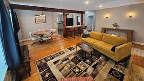 A spacious living room with a yellow sofa, a patterned rug, and a dining area with a wooden table and chairs.
