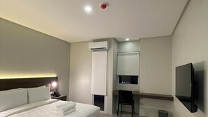 A modern hotel room with a large bed, a desk with a chair, a flat-screen TV, and an air conditioning unit. - Mango Suites Angeles (Angeles City)
