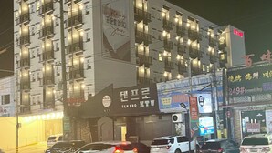 A multi-story hotel with balconies, a large illuminated sign, and various commercial establishments on the ground floor. - Mango Suites Angeles (Angeles City)