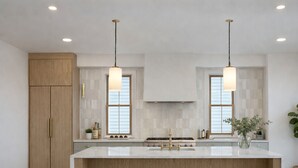 Cozinha moderna com ilha central, iluminação pendente e armário de madeira.