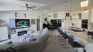 Un salon moderne doté d’un téléviseur à écran plat, d’un canapé, d’un coin repas avec un bar et d’un ventilateur de plafond.