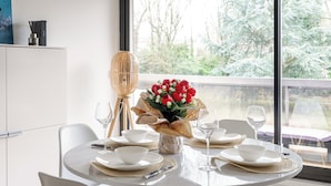Ein Esstisch mit weißen Tellern, Schüsseln und Besteck, einer Vase mit roten Blumen und einem Kerzenständer.