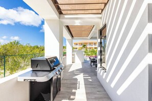 An outdoor balcony with a grill, a dining table, and a view of a building in the background. - Bougain Villa TCI New Luxury Villa Near Grace Bay (Grace Bay)