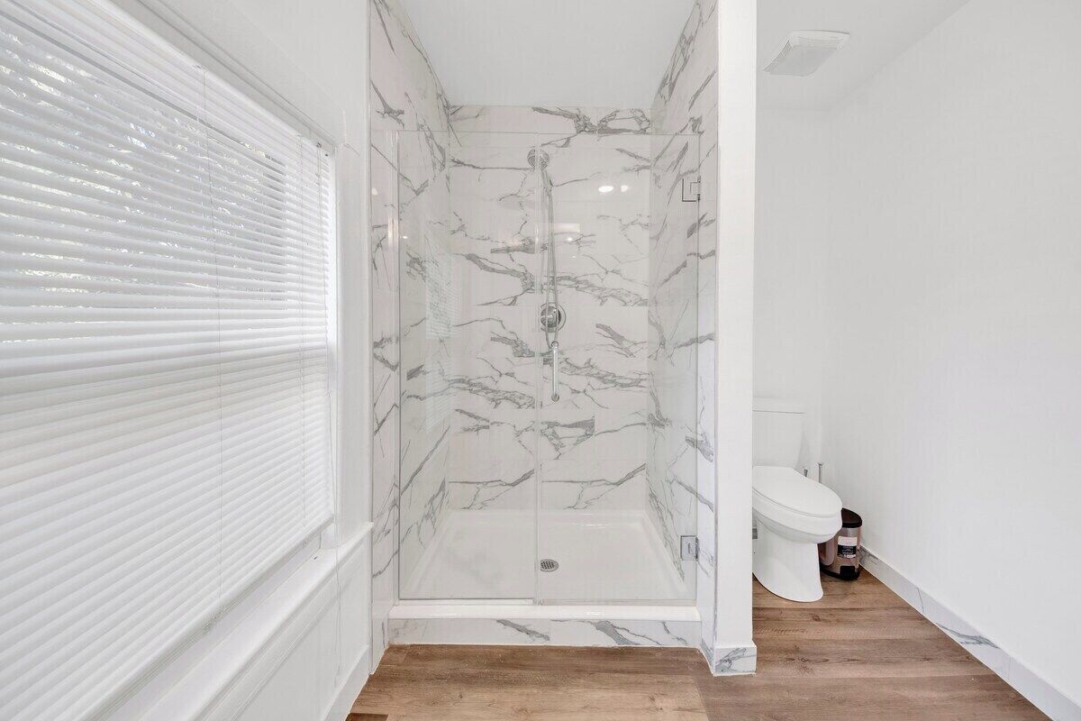 Un baño con ducha de vidrio, inodoro blanco y suelo de madera.