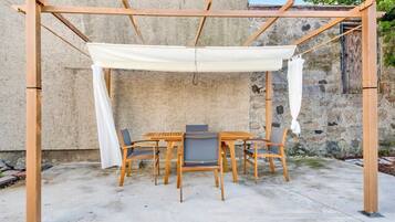 Una pérgola de madera con toldo blanco, una mesa redonda y seis sillas en un entorno al aire libre.