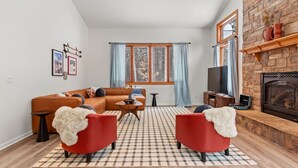 A modern living room with a sectional sofa, two red armchairs, a fireplace, and a large window with curtains. - The Powder Haus: Hot Tub, Sauna, Fire Pit, Golfsim (Wisconsin Dells)