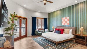 A modern bedroom with a large bed, a desk, and a chair. There is a window with curtains, a ceiling fan, and a wall with a geometric pattern. - The Powder Haus: Hot Tub, Sauna, Fire Pit, Golfsim (Wisconsin Dells)
