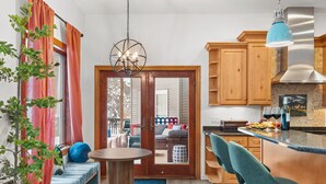 A modern kitchen with wooden cabinets, a central island, and a dining area with blue chairs. - The Powder Haus: Hot Tub, Sauna, Fire Pit, Golfsim (Wisconsin Dells)