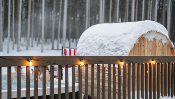 A wooden structure covered in snow, with a wooden fence in the foreground and a snowy forest in the background. - The Powder Haus: Hot Tub, Sauna, Fire Pit, Golfsim (Wisconsin Dells)