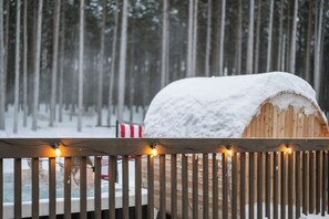 A wooden structure covered in snow, with a wooden fence in the foreground and a snowy forest in the background. - The Powder Haus: Hot Tub, Sauna, Fire Pit, Golfsim (Wisconsin Dells)