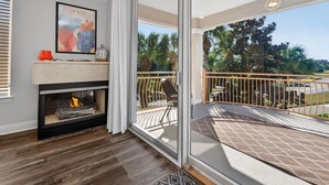 Ein modernes Wohnzimmer mit Kamin, einem Balkon mit Blick auf Palmen und einem großen Fenster.