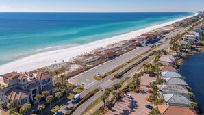 Luftaufnahme einer Küstenwohngegend mit Strand, Häusern und einer Straße.