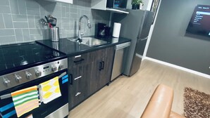 Une cuisine moderne dotée d’appareils électroménagers en acier inoxydable, d’un plan de travail noir et de meubles gris. Le salon est agrémenté d’un canapé en cuir marron.