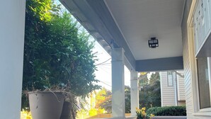 Varanda coberta com rodapé vermelho, colunas brancas e vasos de plantas.
