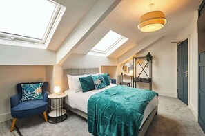 Een moderne slaapkamer met dakraam, een bed met blauwgroene beddengoed, een nachtkastje, een stoel en een hanglamp.