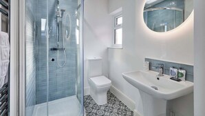 Et moderne badeværelse med en brusekabine i glas, toilet og et spejl over vasken.