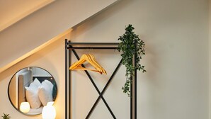 Et værelse med et spejl, en hængende plante, et tøjstativ og et natbord med lampe og fjernbetjening.