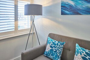 A living room with a grey sofa, two patterned cushions, a floor lamp, and a painting on the wall. - Host Stay The Langley Hotel Apartment 4 (Whitby)