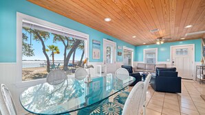 A dining area with a glass table and chairs, a view of the beach, and a ceiling fan. - Bama Breeze | Little Lagoon w/ Fishing Dock | Dog Friendly | My Beach Getaways (Gulf Shores)