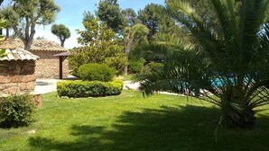 Un jardín bien cuidado con una estructura de piedra, una palmera y diversos arbustos.