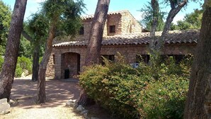 Un edificio de piedra con techo de tejas, rodeado de árboles y arbustos.
