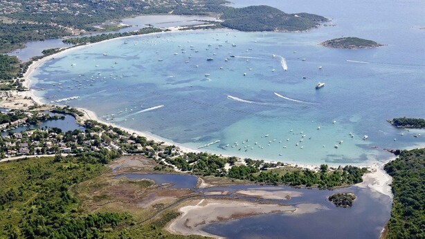 Vista aérea de una zona costera con un puerto deportivo, playas de arena y vegetación circundante.
