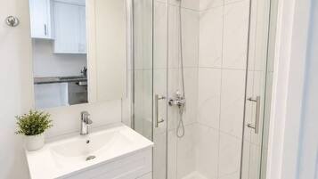 A modern bathroom with a glass-enclosed shower, a white sink, and cabinets.