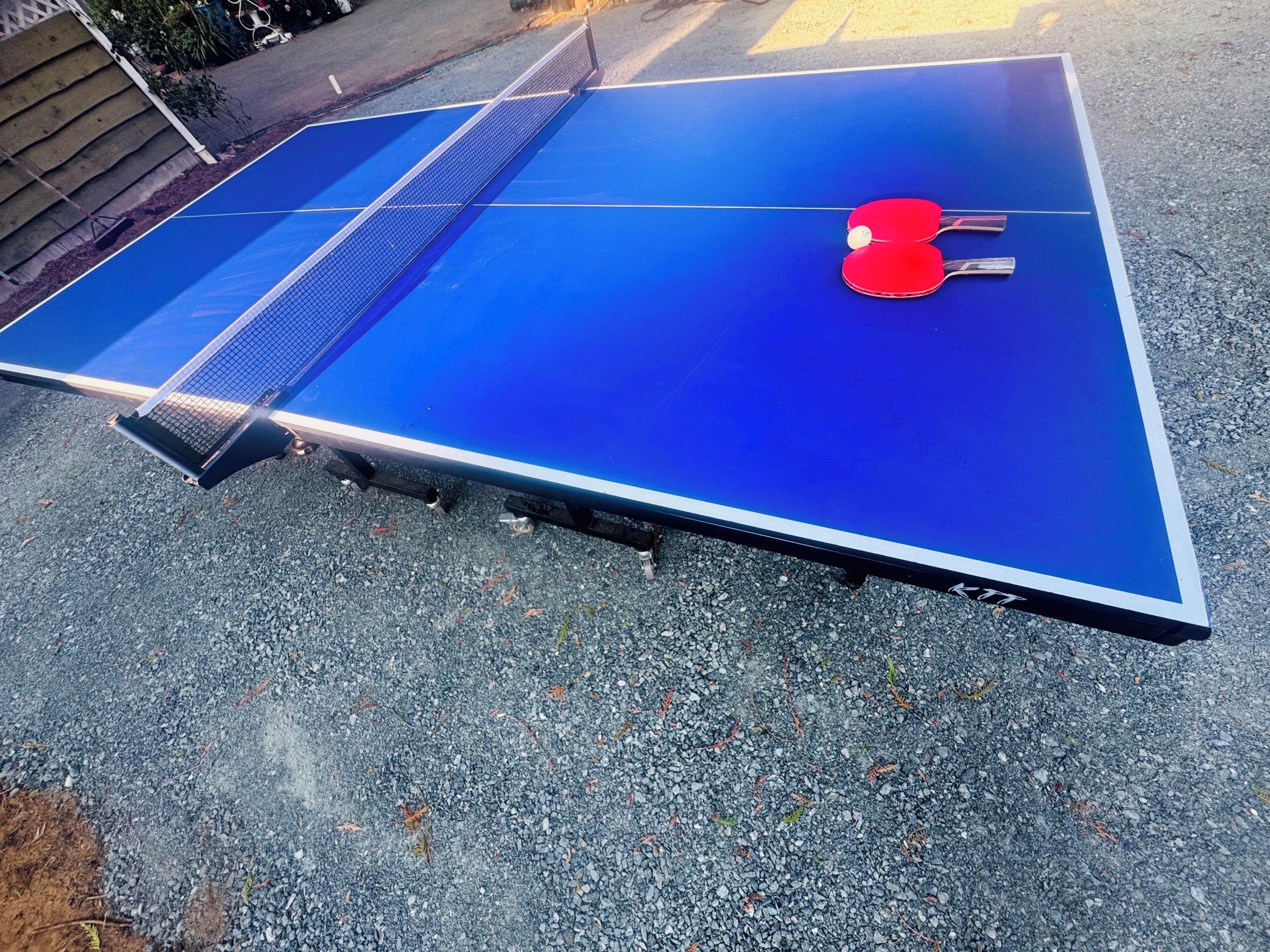 Ein blauer Tischtennis-Tisch mit zwei roten Schlägern und einem Netz in der Mitte.