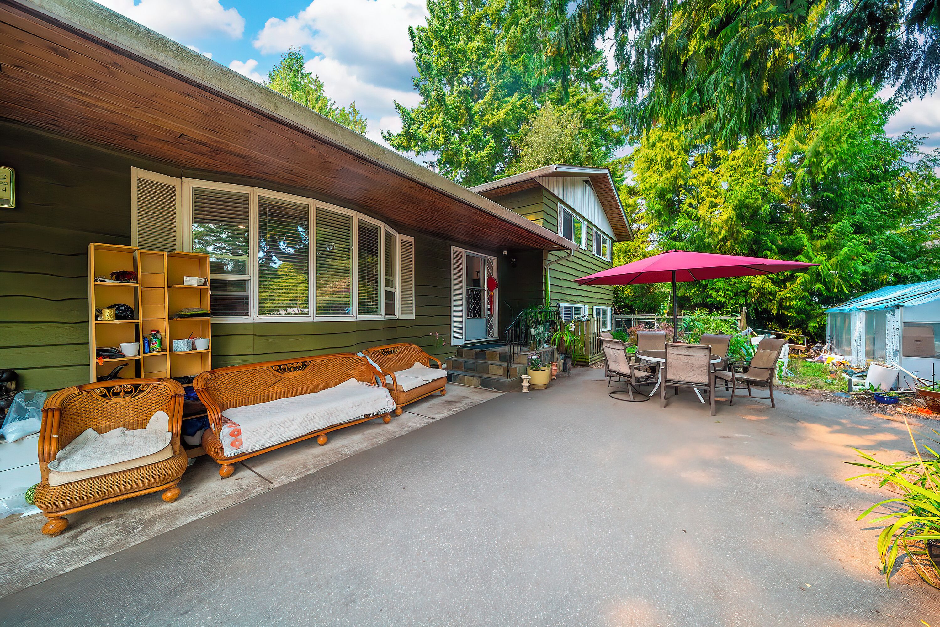 Une maison dotée d’un porche abrité, de meubles en osier et d’un coin repas avec une table et des chaises.