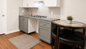 A compact kitchen with a gas stove, a sink, and a small dining area with a table and chairs. - Cozy 3BR Villa Garden View Beach (Surrey)