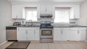A kitchen with white cabinets, a stainless steel dishwasher, a toaster, a sink, and a double oven. - Cozy 3BR Villa Garden View Beach (Surrey)
