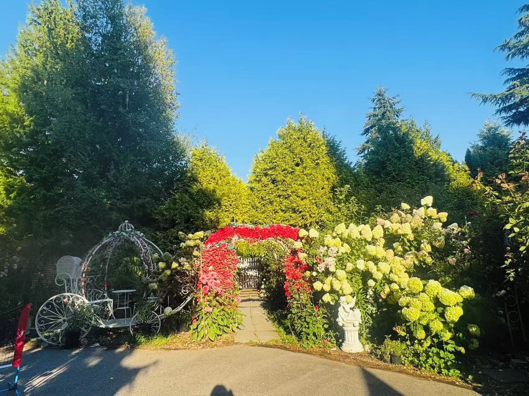 A garden pathway with a decorative archway, a metal bench, and a statue.
