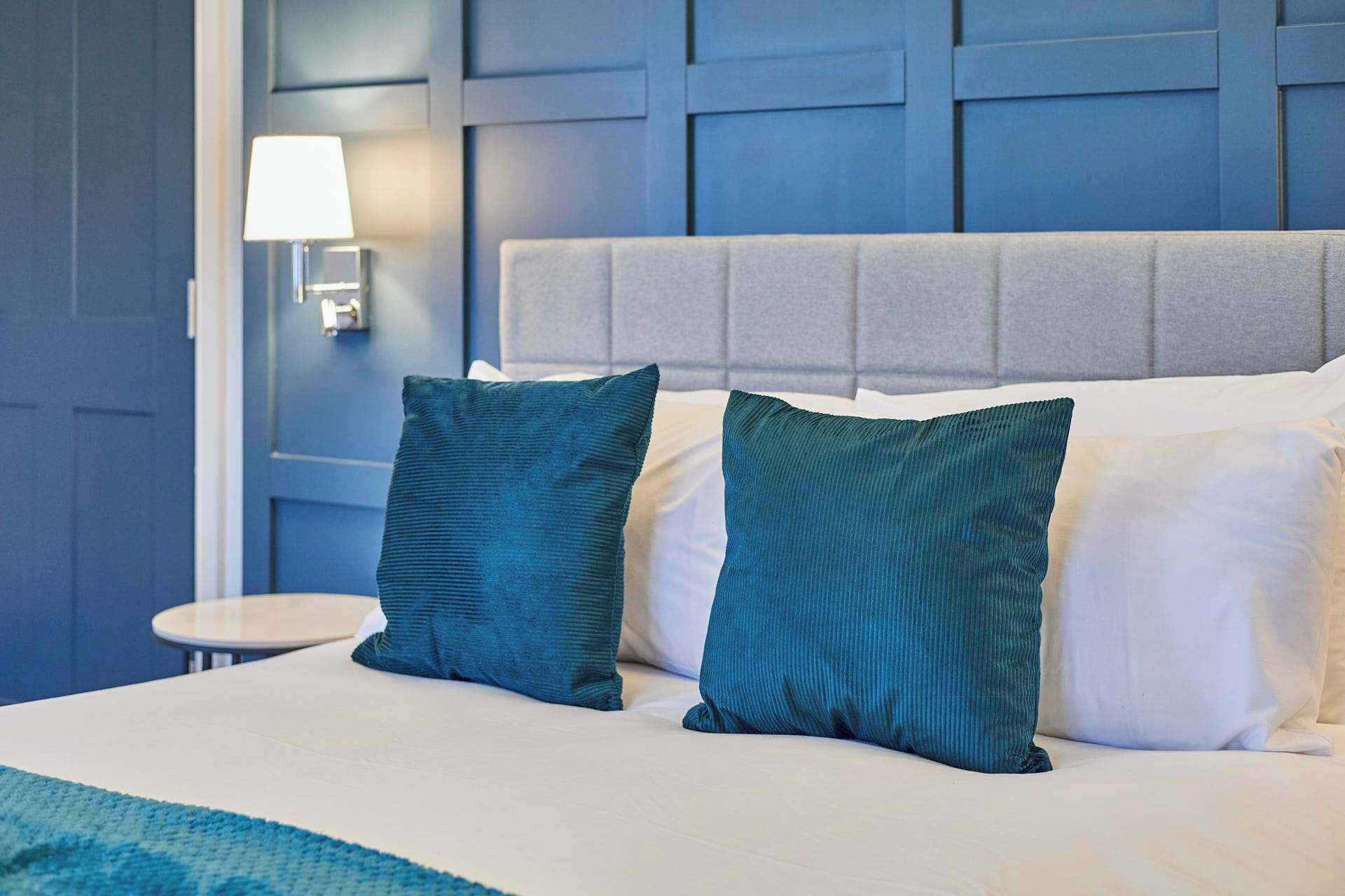 A bed with two teal pillows, a white pillow, and a grey headboard.