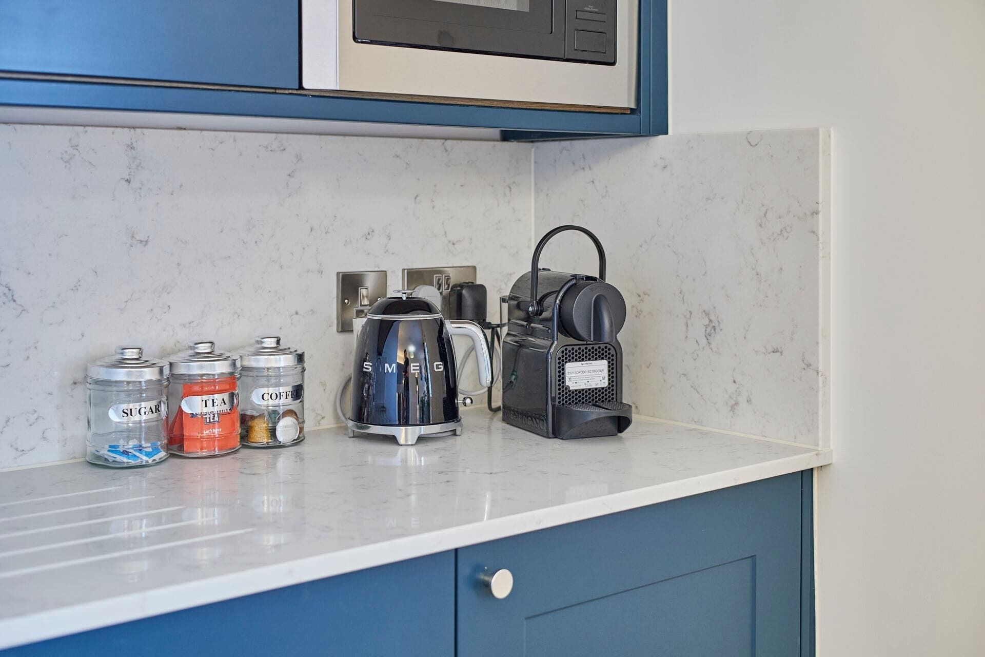 A kitchen counter with a coffee maker, sugar, tea, and coffee containers.