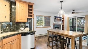 Una cocina con armarios de madera, lavavajillas, zona de comedor con taburetes y un ventanal con vistas a árboles.