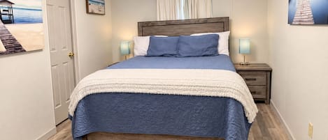 A bedroom with a wooden bed, a white door, and a nightstand with a lamp.