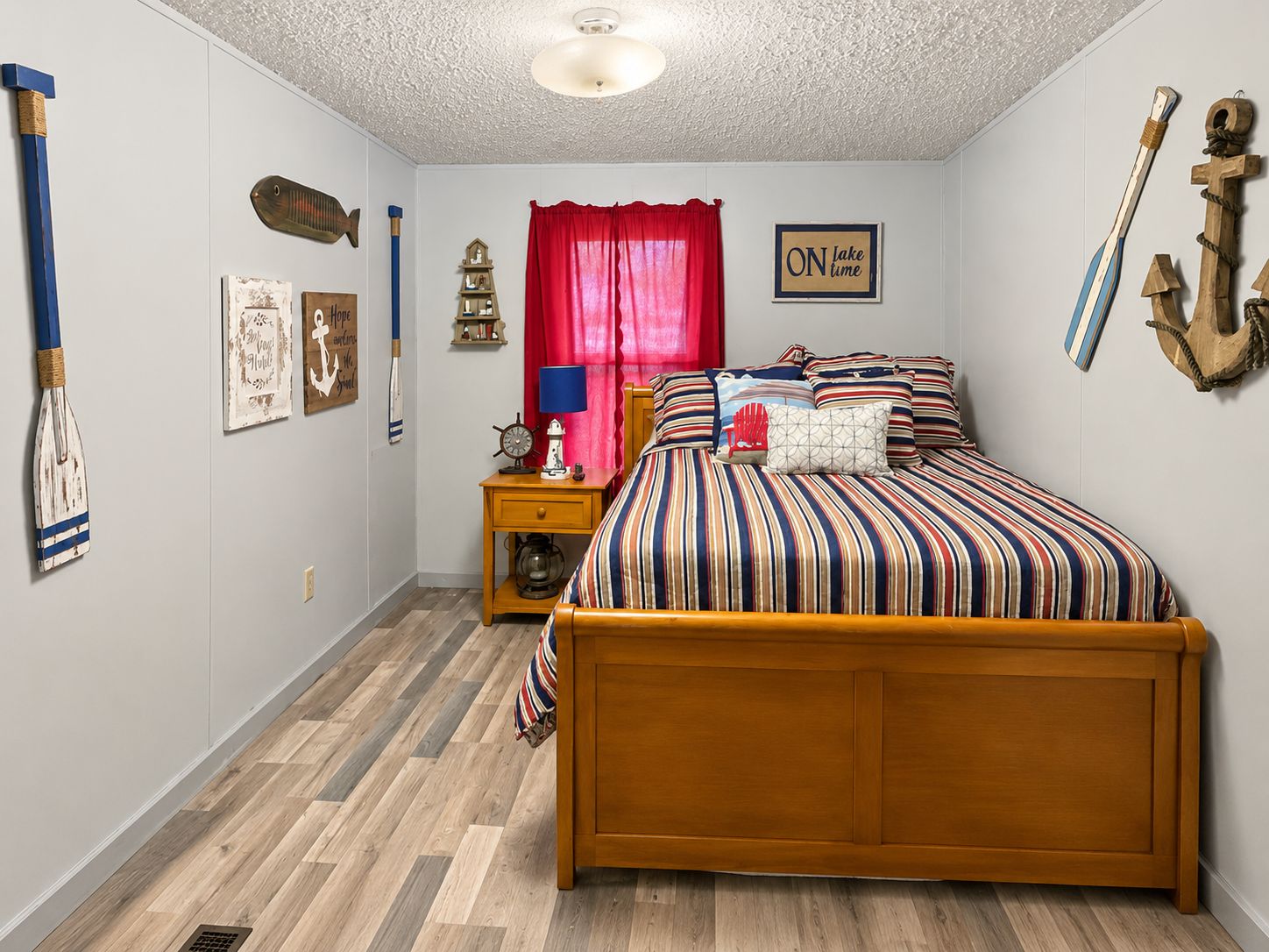 A bedroom with a wooden bed, a nightstand with a lamp, a red curtain, and nautical-themed decorations.