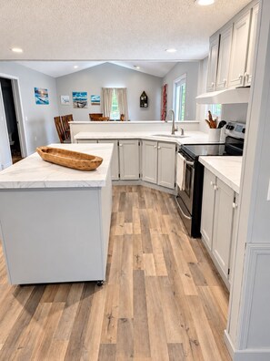 A modern kitchen with a large island, white cabinetry, and a herringbone wood floor. - 4-bedrooms, Cherokee Lake Retreat — Close to the Smokies, Away from the Crowds (Bean Station)