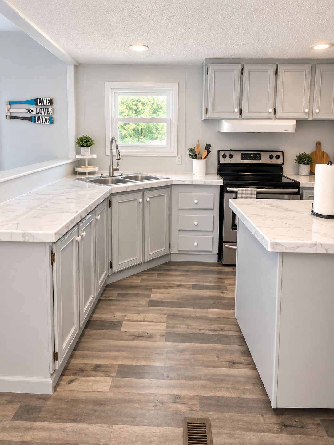 A kitchen with white cabinets, a double sink, a stove, and a window with a view of greenery.