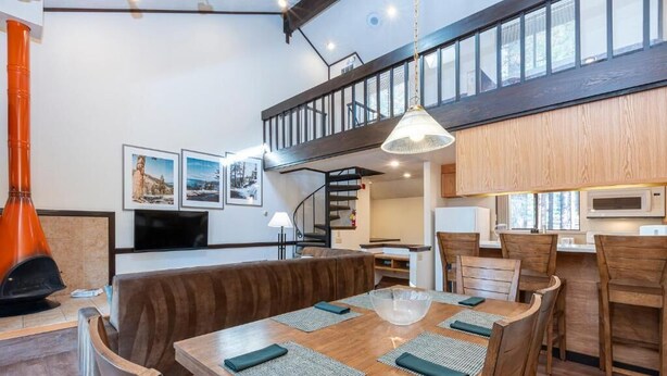Un comedor moderno con una mesa de madera, sillas y un tazón grande. Una escalera conduce a un nivel superior.