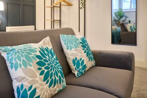 A grey sofa with two teal leaf-patterned cushions. - Host Stay The Langley Hotel Apartment 12 (Whitby)