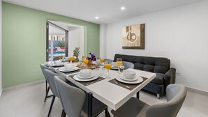 Un coin repas avec une table dressée pour quatre personnes, entourée de chaises, et un canapé en arrière-plan.
