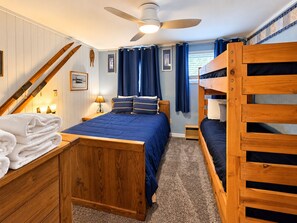 Ein Zimmer mit einem Etagenbett, einem Einzelbett, einem Deckenventilator und einer Treppe.