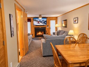 A cozy living room with a fireplace, a television, and a dining area with wooden furniture. - Powderidge 42 2 Br: Sleeps 10 (Snowshoe)