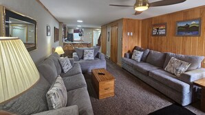 Un salon avec deux canapés gris, une table basse en bois, une lampe et un ventilateur de plafond.