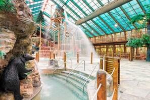 An indoor water feature with a waterfall, surrounded by wooden benches and a bear statue. - 2BR Mountain Cabin with Balcony, Fireplace & Tub in lovely Gatlinburg (Gatlinburg)