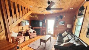 A wooden interior with a sofa, armchairs, a coffee table, a TV, and a fireplace.