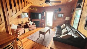 Un intérieur en bois comprenant un canapé, des fauteuils, une table basse, un téléviseur et une cheminée.